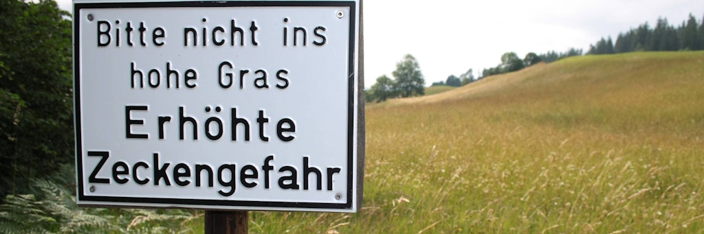 Ein Warnschild warnt vor Zecken im Gras.