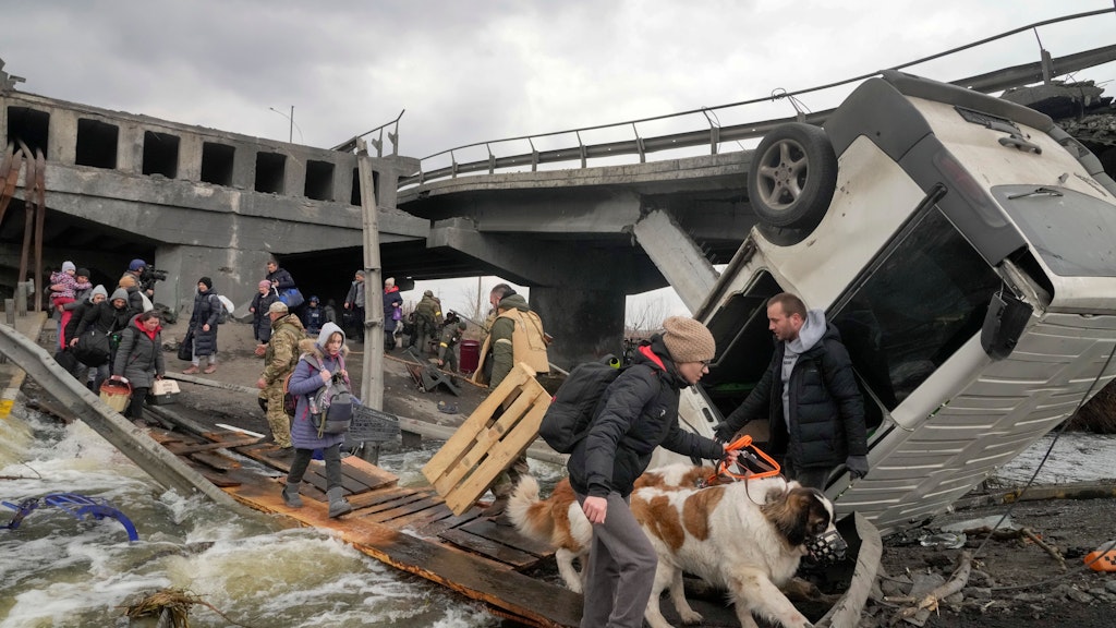 Irpin: Menschen überqueren einen improvisierten Weg unter einer zerstörten Brücke auf der Flucht aus der Stadt Irpin in der Nähe von Kiew. Eine Frau hat ihre Hunde dabei, eine andere trägt einen Katzenkorb mit sich.