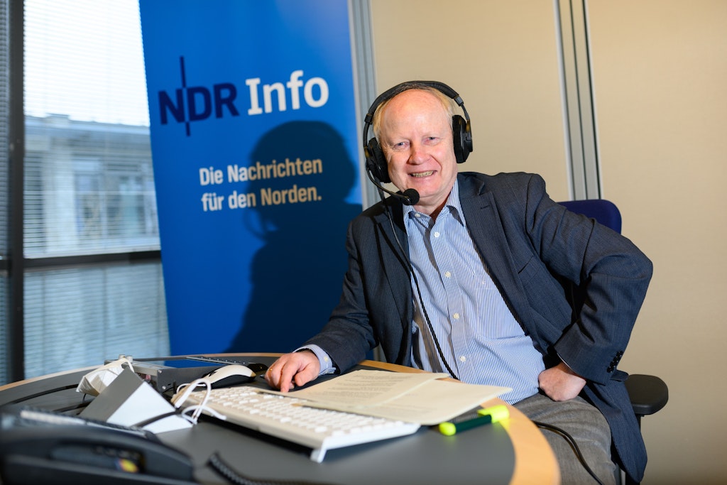 NDR-Sicherheitspolitikexperte Andreas Flocken spricht in einem Aufnahmestudio vor dem Logo des Nachrichtenformats. Seinen Podcast "Streitkräfte und Strategien" wollen viele Menschen hören.