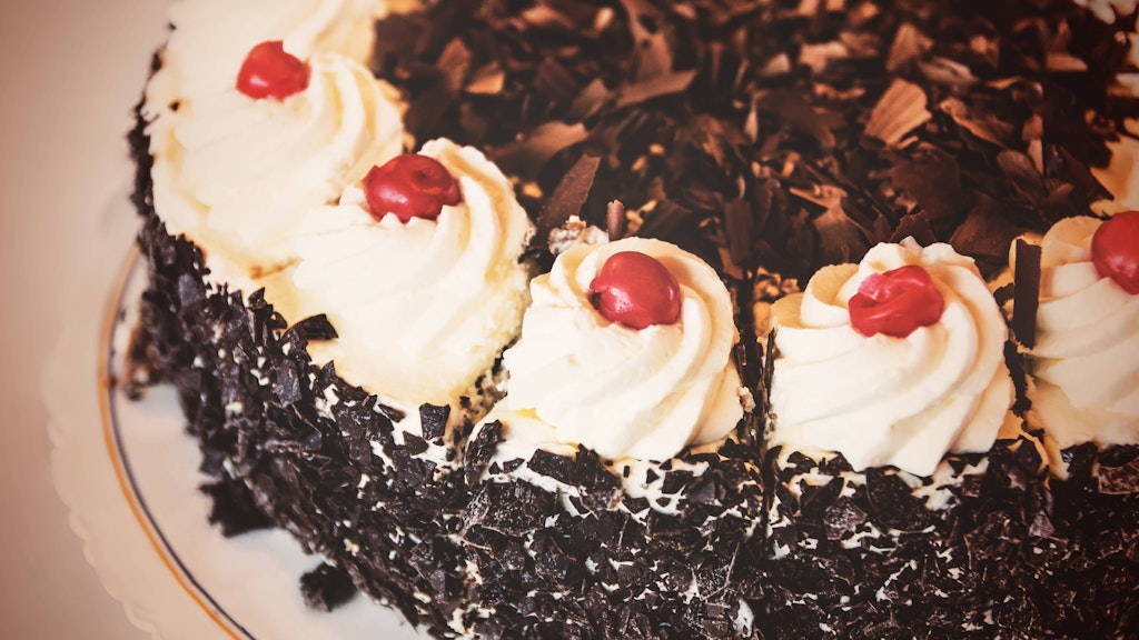 Die Schwarzwälder Kirschtorte wird klassisch mit Schlagsahne, Schokoraspeln und Belegkirschen verziert.