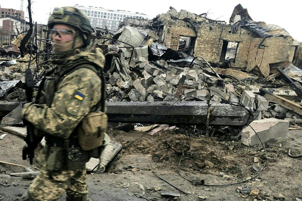 Ein ukrainischer Soldat läuft in Butscha an den Trümmern zerstörter Häusern vorbei.