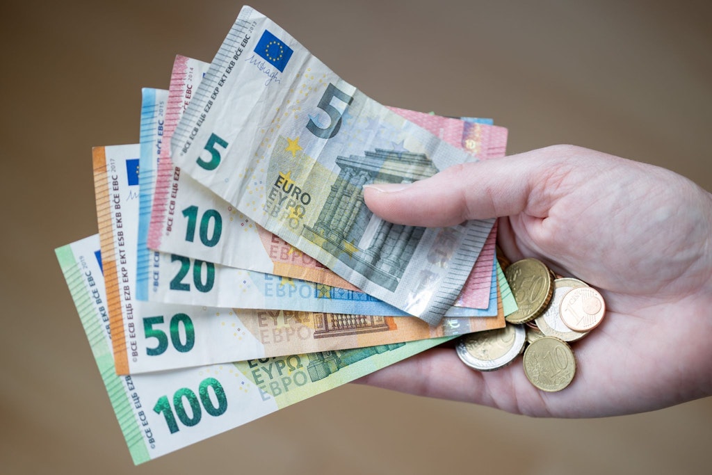 Eine Frau hält Geldscheine und Münzen in der Hand. Eine große Studie belegt: Zeige mir, wo du wohnst – und ich sage dir, wie viel Geld du hast!