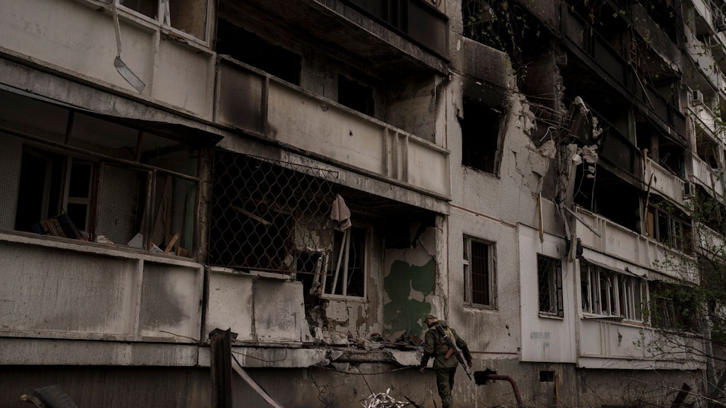 Ein ukrainischer Soldat steht nach einem russischen Angriff vor einem beschädigten Wohnhaus.
