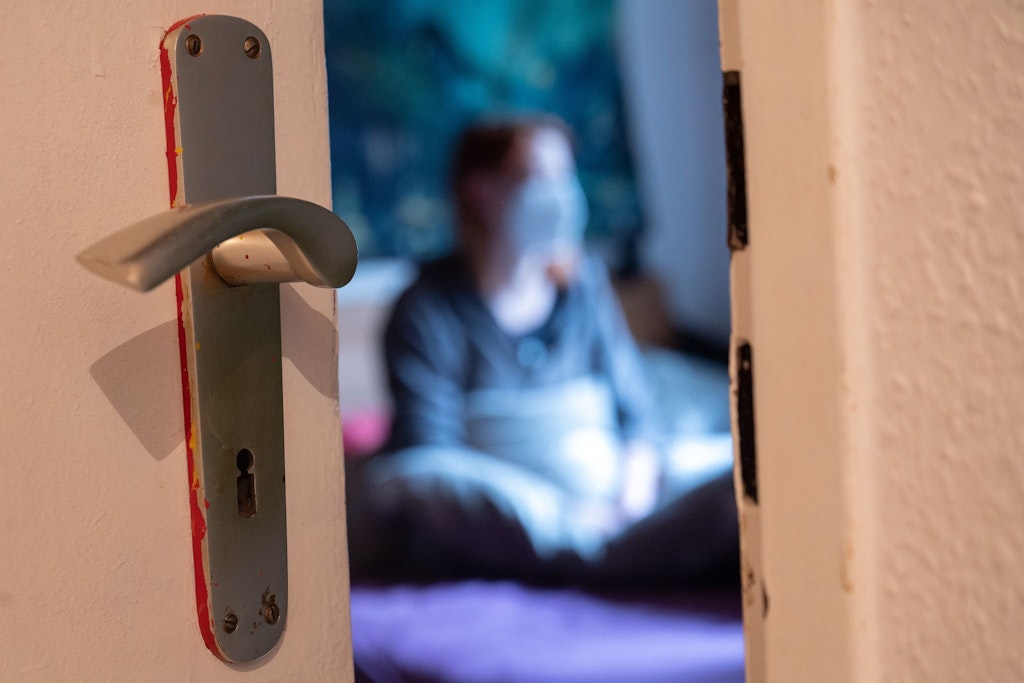 Eine Frau sitzt während der Isolation nach einem positiven Corona-PCR-Test auf ihrem Bett. Die Dauer der Isolation soll verkürzt werden. Darauf einigten sich die Gesundheitsminister von Bund und Ländern.