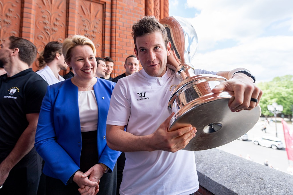 Eisbären-Torjäger Matt White schleppt den Pokal auf dem Rathaus-Balkon, Berlins Regierende Bürgermeisterin Franziska Giffey hat sichtlich Spaß daran.