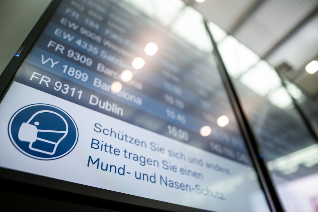 Auf einer Anzeigetafel im Flughafen Düsseldorf steht der Hinweis „Schützen Sie sich und andere. Bitte tragen Sie einen Mund- und Nasen-Schutz“