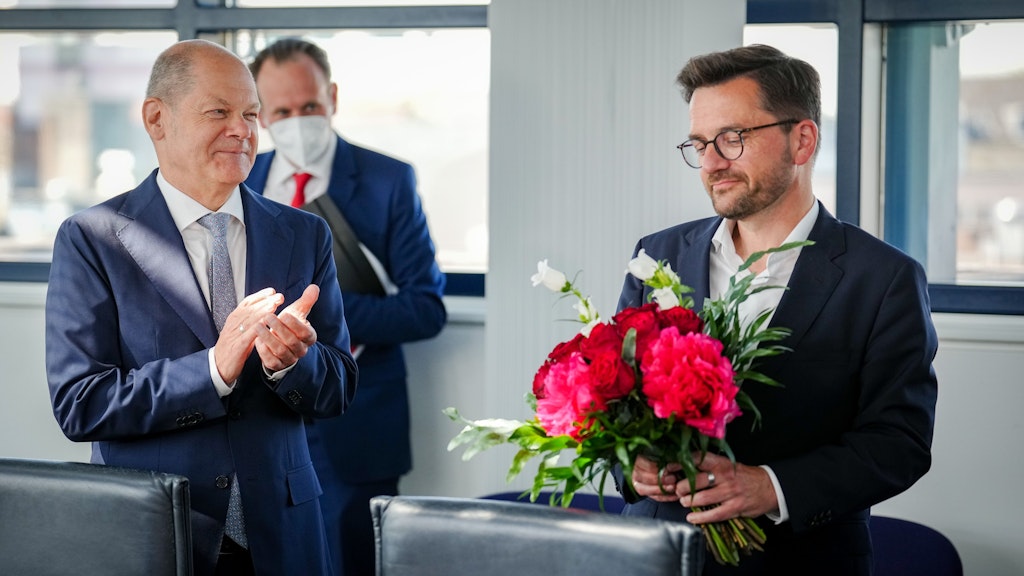 Versonnen blickt Thomas Kutschaty auf einen Blumenstrauß, während Kanzler Scholz dem Wahlverlierer bei der SPD-Präsidiumssitzung am Montag in Berlin applaudiert.