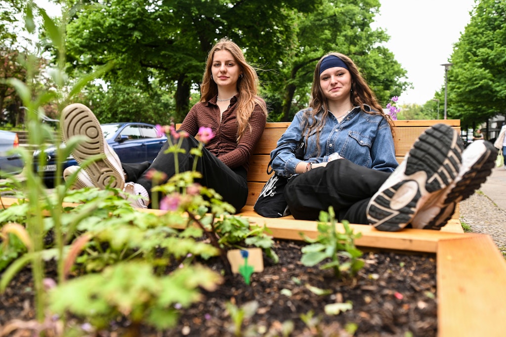 Olga (18) aus Prenzlauer Berg und Anouk (18) aus Köpenick, die auf der Holzbank am Petersburger Platz nach einer Abitur-Prüfung chillen, sind begeistert vom neuen Rastplatz. „Wir können hier gemütlich essen, sind für uns und doch mittendrin“, sagen sie.
