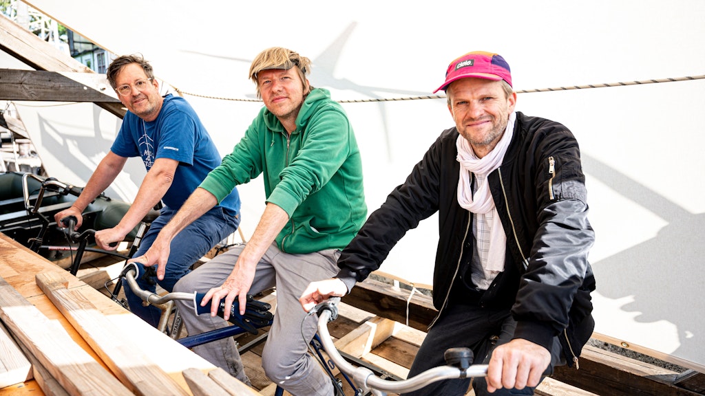 Das Künstler-Trio Philip Horst (v.l.), Harry Sachs und Matthias Einhoff treten auf dem Schiff „Citizenship“ in die Pedale der angebrachten Fahrräder.