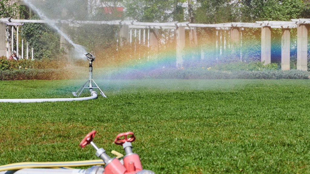 Die Wassertropfen eines Rasensprengers erzeugen eine Lichtreflexion in Regenbogenfarben. Sprengen ist nicht die optimale Form des Gießens.