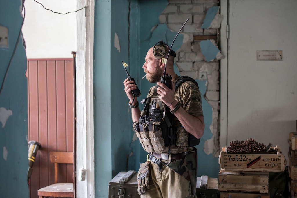 Zwei Funkgeräte in der Hand, Kopfhörer hochgeschoben, Zigarette im Mund: Ein ukrainischer Soldat versucht während der Schlacht um Sjewjerodonezk, den Überblick zu behalten. Links lehnt eine Panzerabwehrwaffe an der Wand, rechts stehen Munitionskisten.
