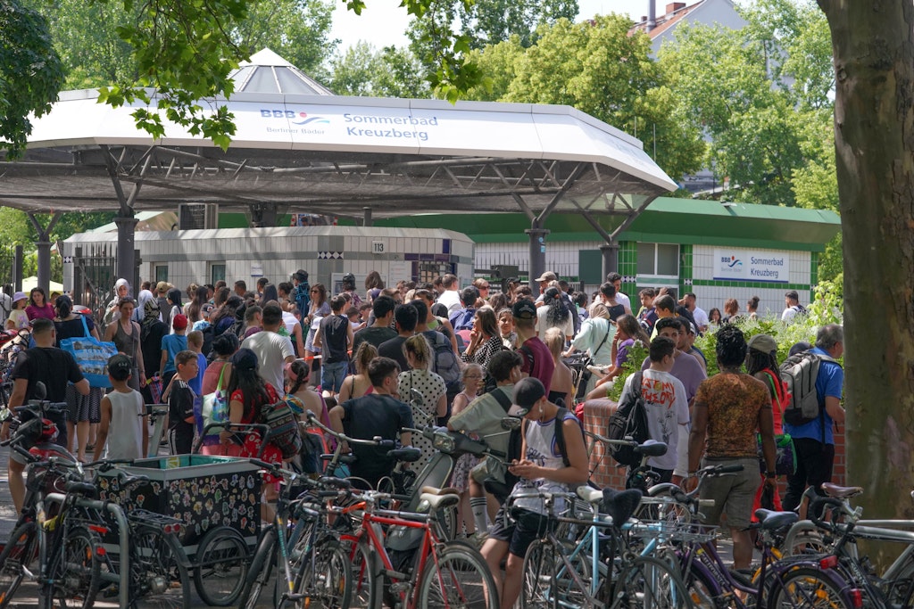 Zahlreiche Menschen warten bei hochsommerlichen Temperaturen auf Einlass ins Sommerbad Kreuzberg.