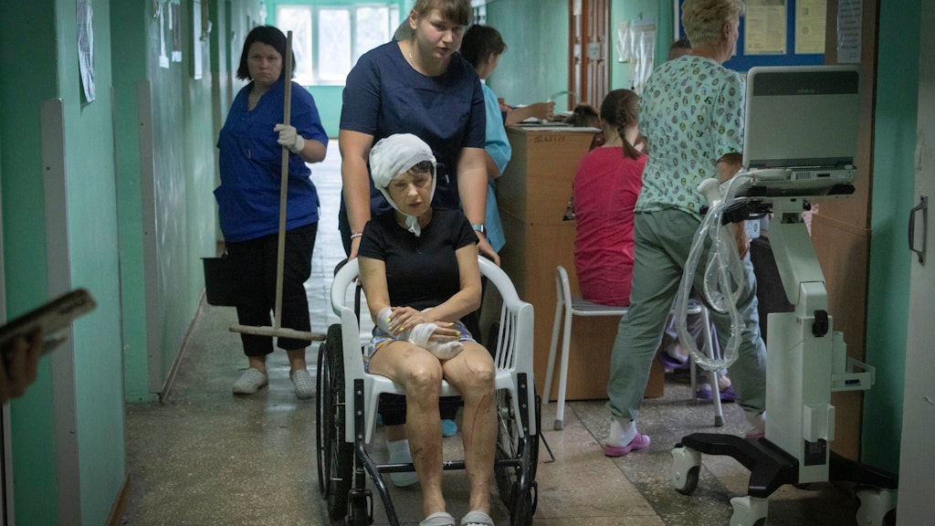 Eine Krankenschwester schiebt eine beim Raketenangriff auf das Einkaufszentrum von Krementschuk verletzte Frau im Rollstuhl.
