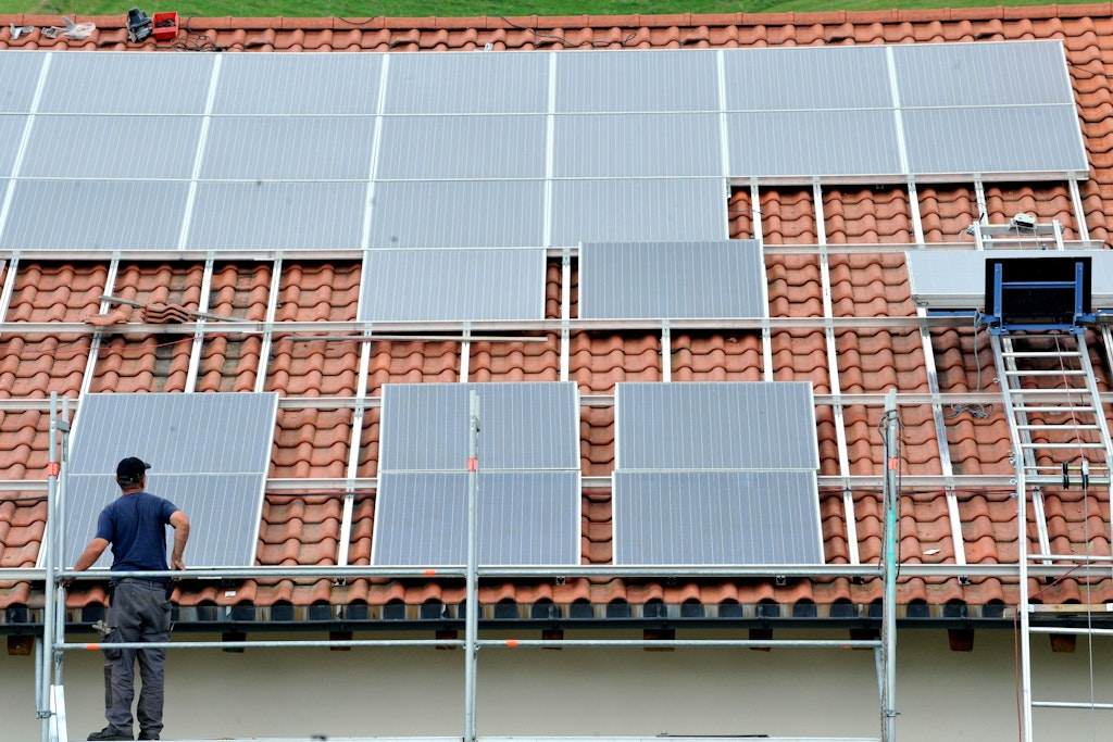 Ein Arbeiter installiert auf einem Dach eine Solaranlage.