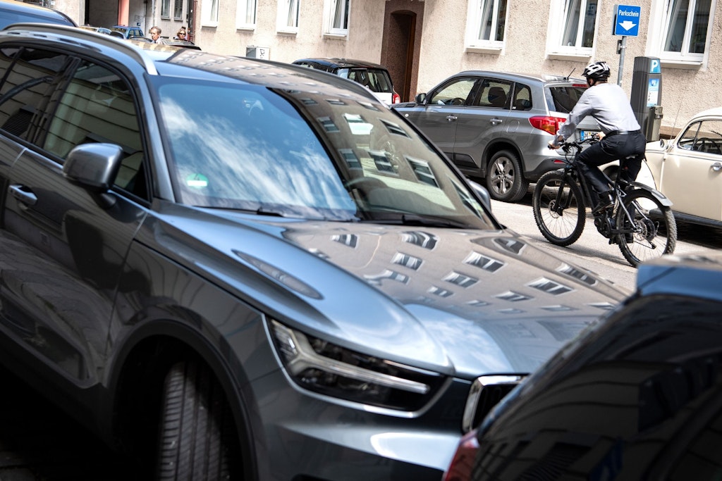 Ein SUV steht am Straßenrand, dahinter fährt ein Fahrradfahrer auf der Straße.