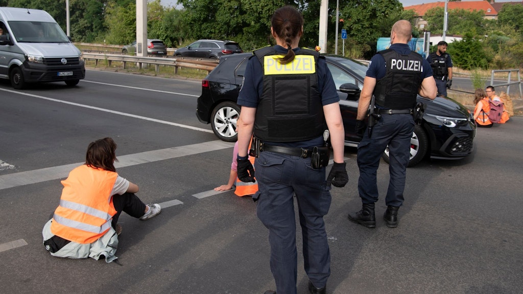 Polizeibeamte stehen bei den Demonstranten der Gruppe „Letzte Generation“ auf einer Kreuzung.