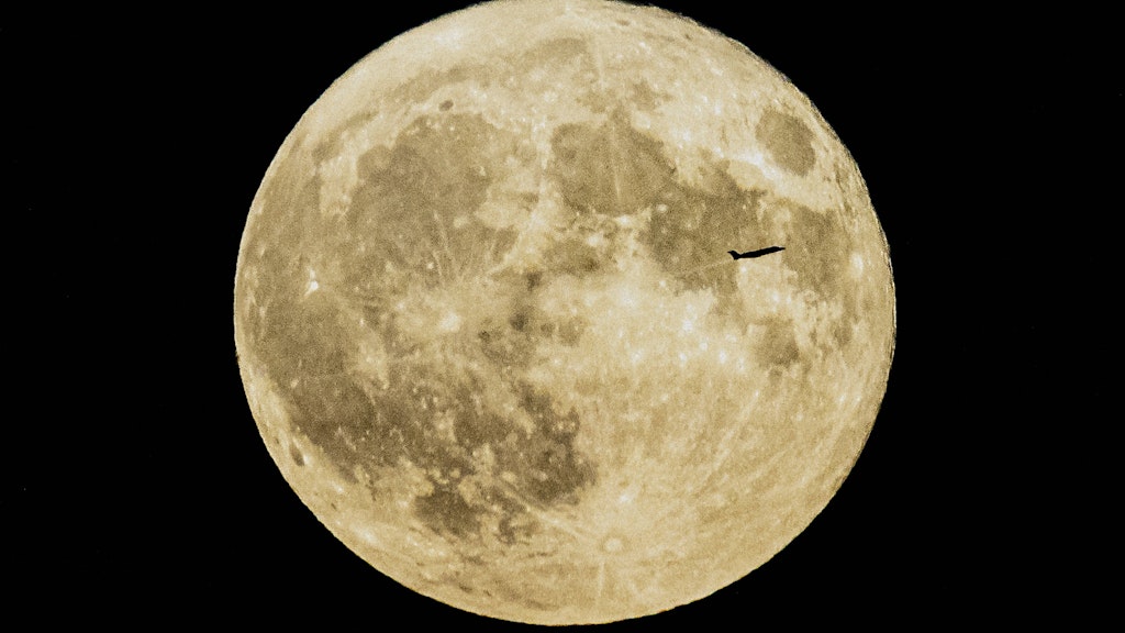 Ein Flugzeug zeichnet sich bei Start vor dem sogenannten Erdbeermond ab.