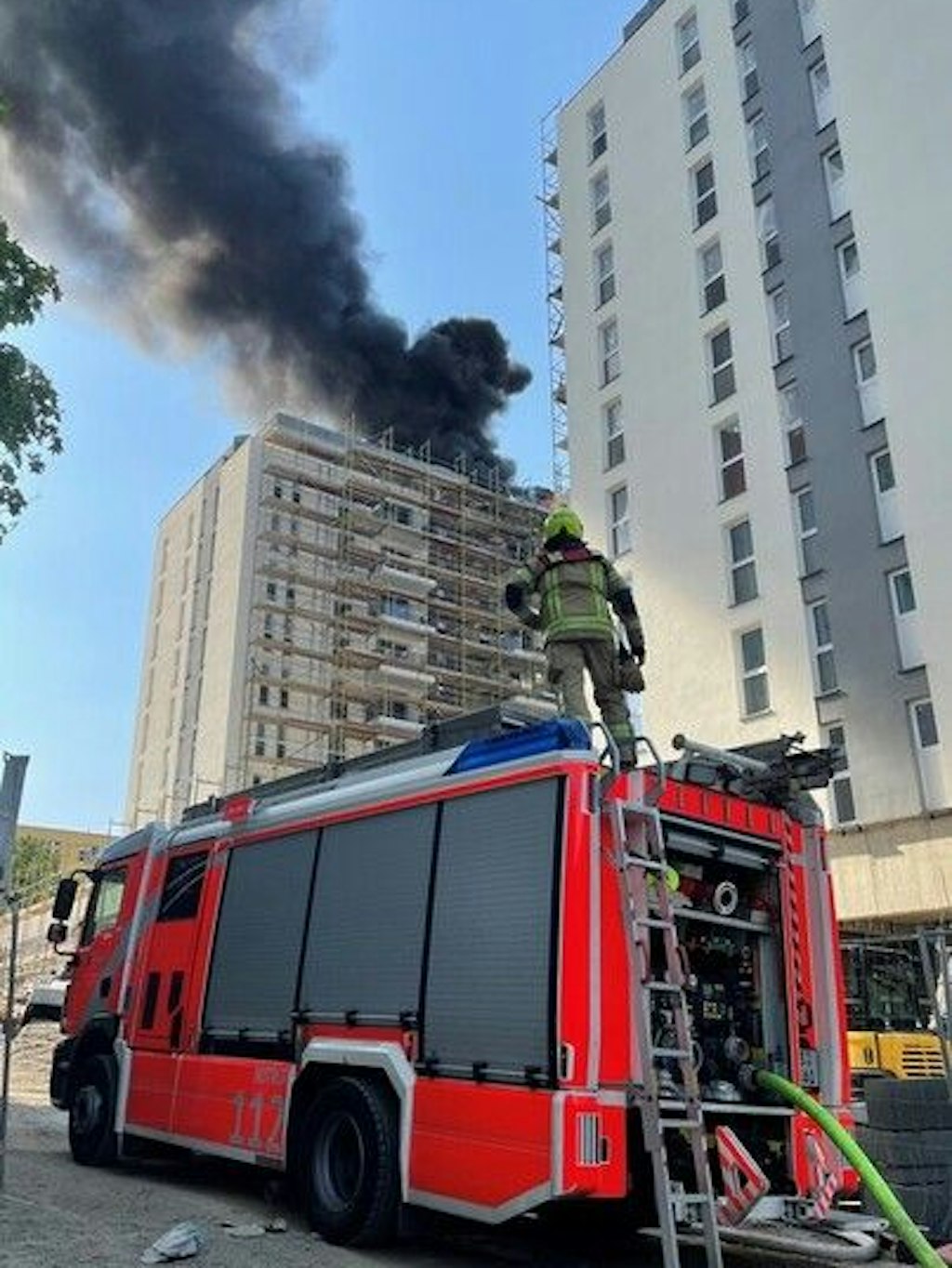 Eine schwarze Rauchsäule steigt vom Dach des berennenden Hochhauses auf.