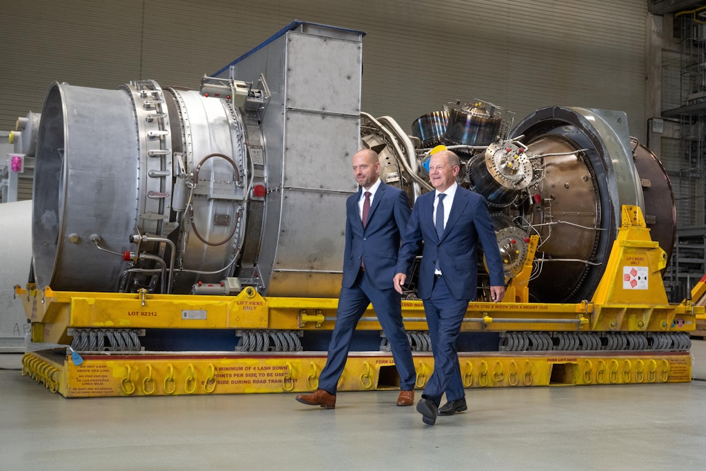 Bundeskanzler Olaf Scholz geht mit dem Chef von Siemens Energy an der Turbine vorbei, die in Mülheim/Ruhr auf ihren Weitertransport nach Russland wartet.