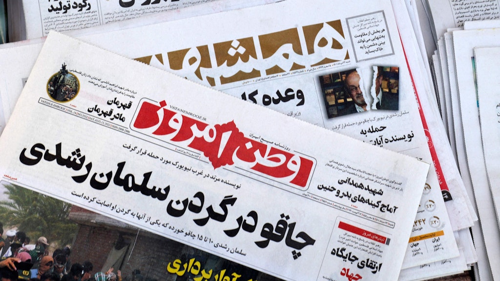 Die Titelseiten der iranischen Zeitungen vom 13. August: Vatan-e Emrooz (vorne) mit dem Titel „Messer im Nacken von Salman Rushdie“ und Hamshahri (hinten) mit dem Titel „Angriff auf den Autor der satanischen Verse“, kombiniert mit einem zerrissenen Foto von Rushdie.