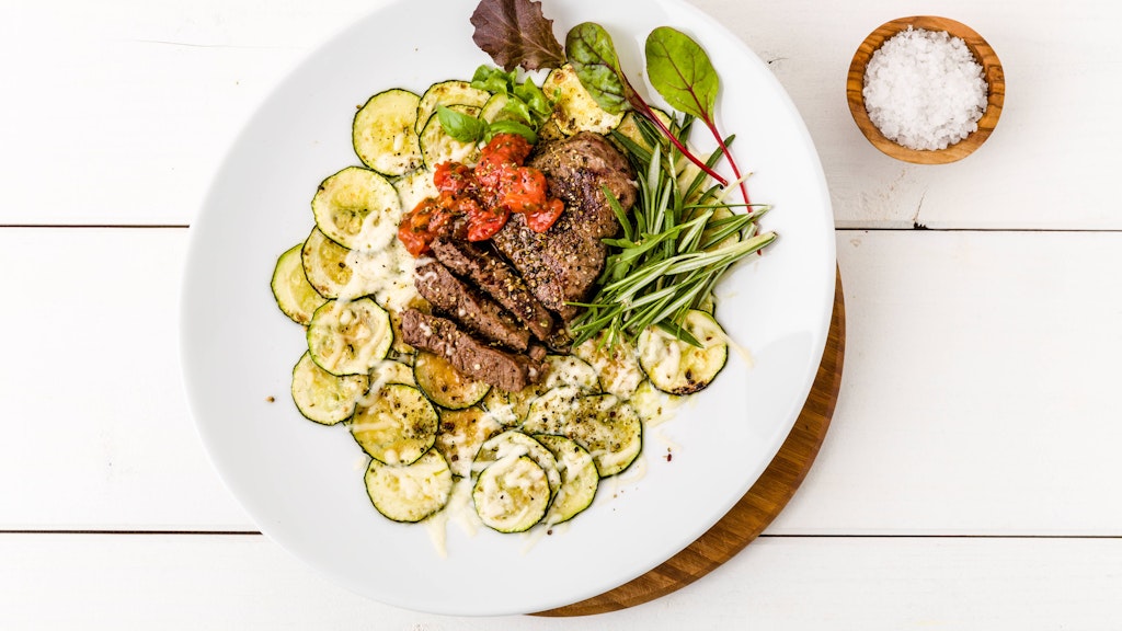 Überbackene Zucchini-Scheiben sind die perfekte Beilage zum Fleisch, schmecken aber als leichtes Abendbrot an heißen Tagen auch pur einfach lecker.