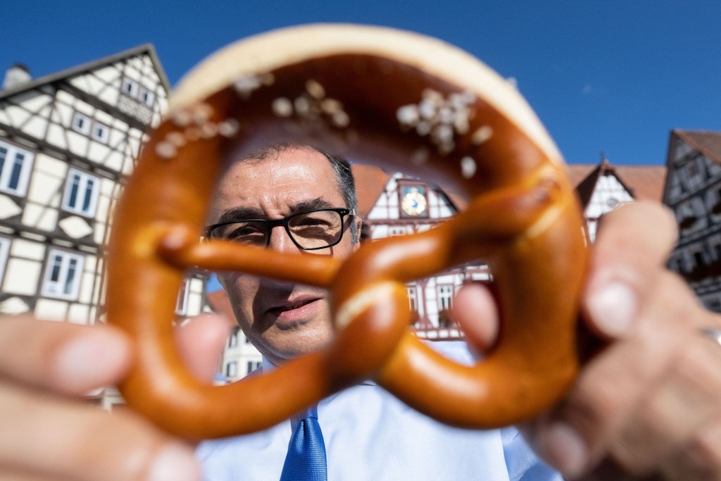 Bundeslandwirtschaftsminister Cem Özdemir (Bündnis 90/Die Grünen) schaut in seiner schwäbischen Heimat durch eine Brezel. 
