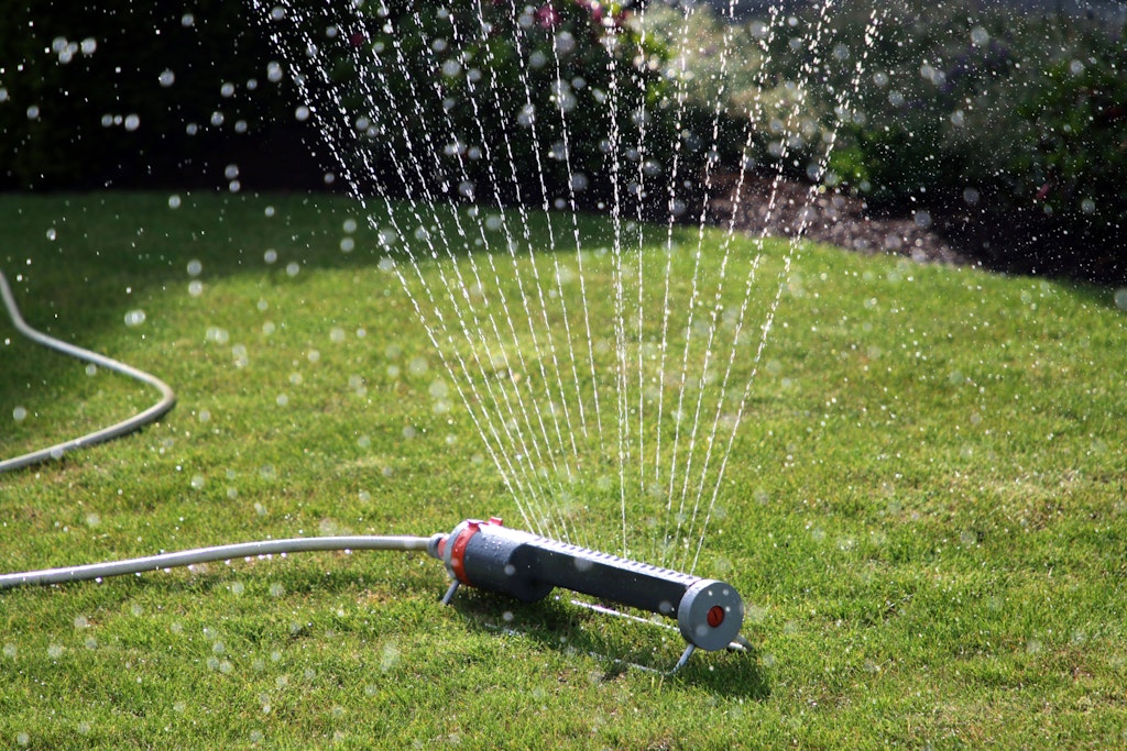 Ein Rasensprenger verteilt Wasser auf eine größere Rasenfläche, die unter der bestehenden Trockenheit leidet. 