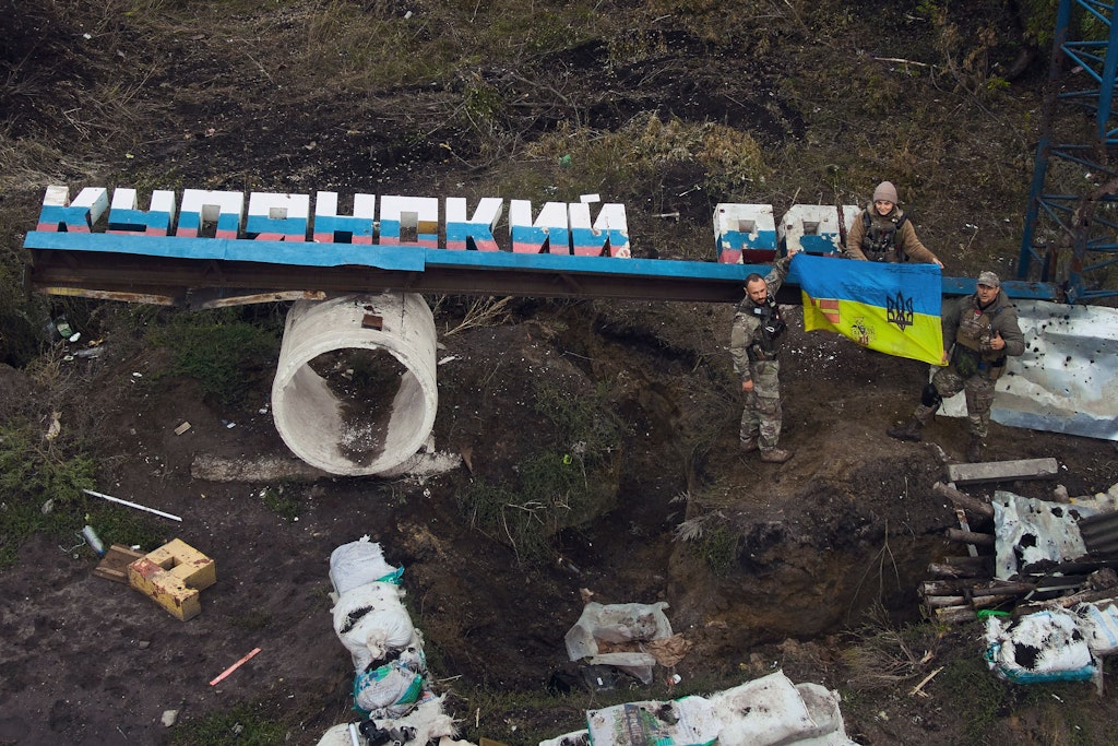Ukrainische Soldaten halten eine ukrainische Fahne auf dem beschädigten Schild "Bezirk Kupiansk" in der Nähe der kürzlich zurückeroberten Stadt Kupjansk in der Region Charkiw. 