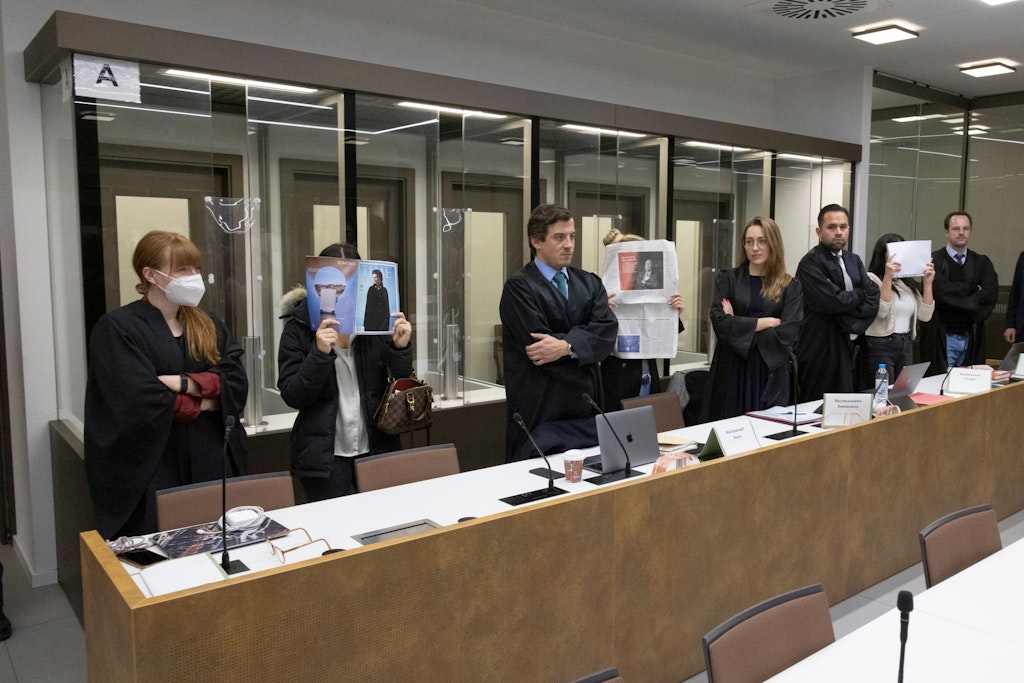 Die Angeklagten verdecken ihre Gesichter, daneben stehen die Anwälte. 