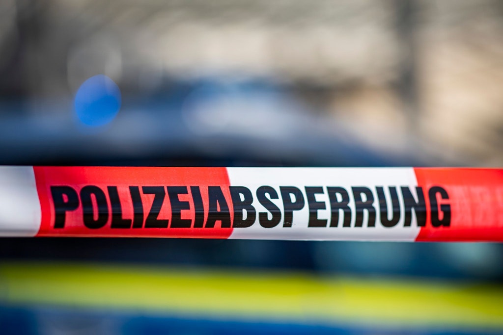 Ein Absperrband mit der Aufschrift „Polizeiabsperrung“ ist vor einem Polizeiwagen aufgespannt. 