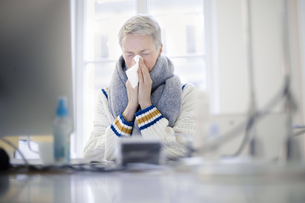 Eine Frau sitzt mit Schnupfen im Büro.