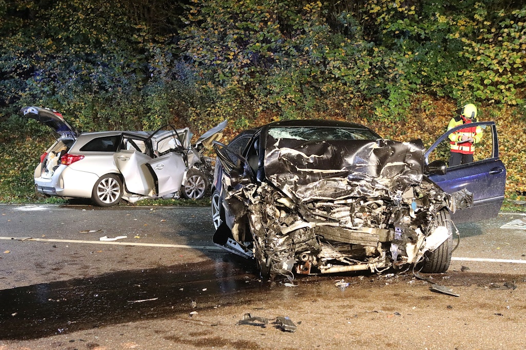 Ein Feuerwehrmann steht nach dem schweren Unfall zwischen den beiden stark zerstörten Wracks.
