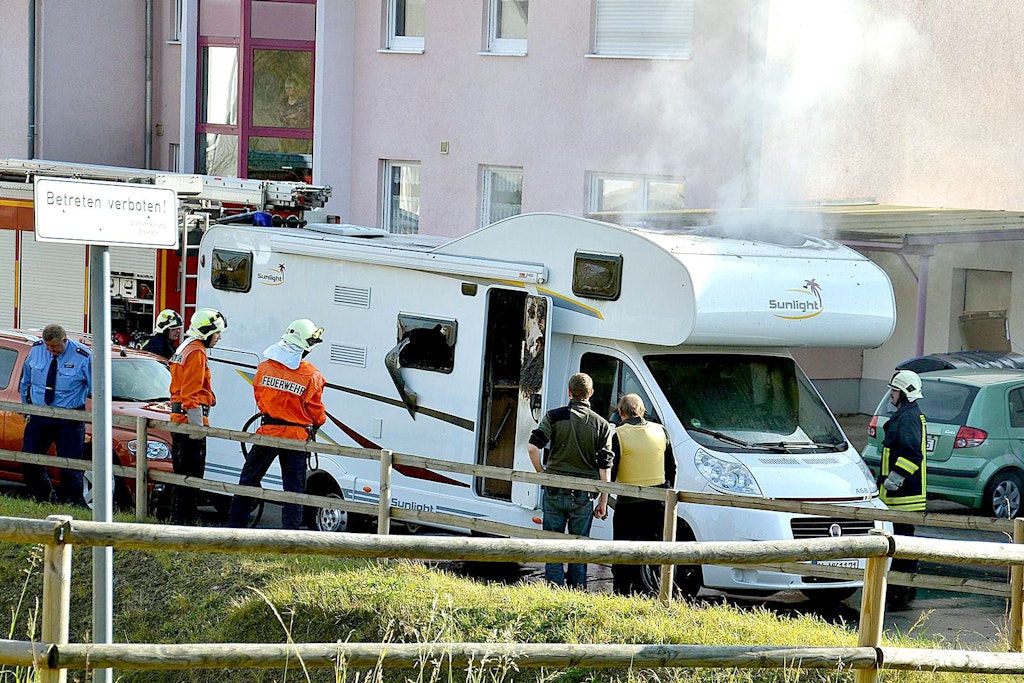 Feuerwehrleute und Polizisten stehen am Wohnmobil in dem sich die NSU-Terroristen Uwe Mundlos und Uwe Böhnhardt selbst getötet haben.