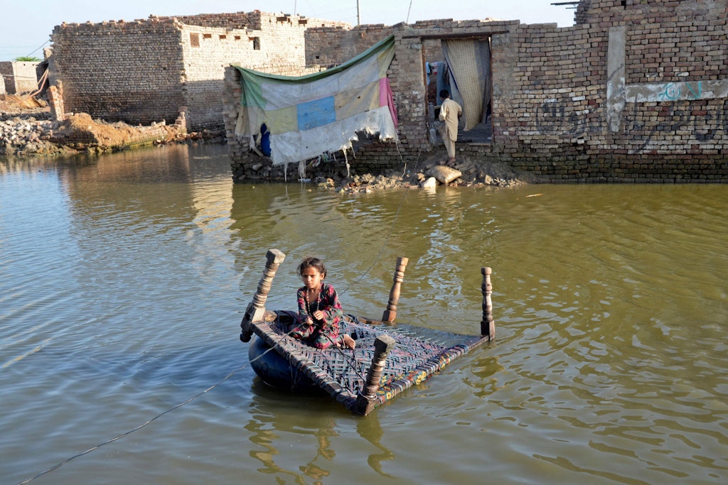 Ein Bett als Fähre: Ein Mädchen überquert eine überflutete Straße in der pakistanischen Region Jafarabad.
