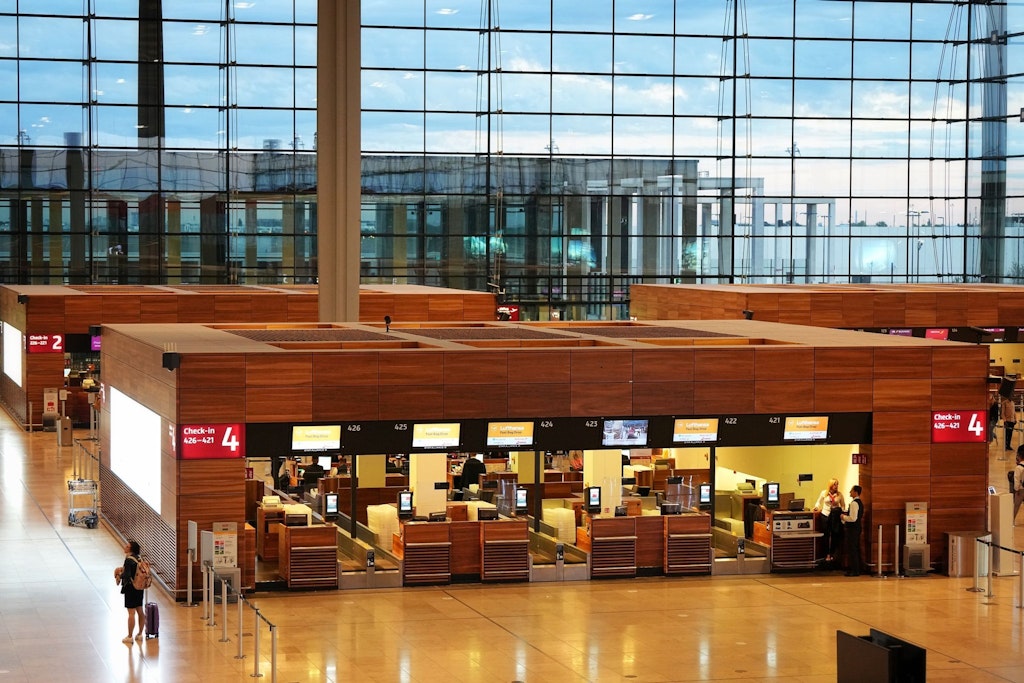 Check-in-Schalter im Terminal 1 auf dem Flughafen Berlin Brandenburg. Im Hintergrund die großen Glasfassaden des Baus. 