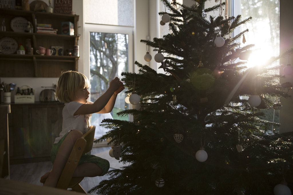 Ein Mädchen dekoriert den Christbaum. Früher mussten Kinder vor der Stube warten, bis sie gerufen wurden und sahen erst dann den Baum. 