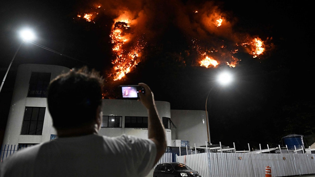 Ein Mann macht ein Foto von dem Feuer auf einem der Hügel Rios.