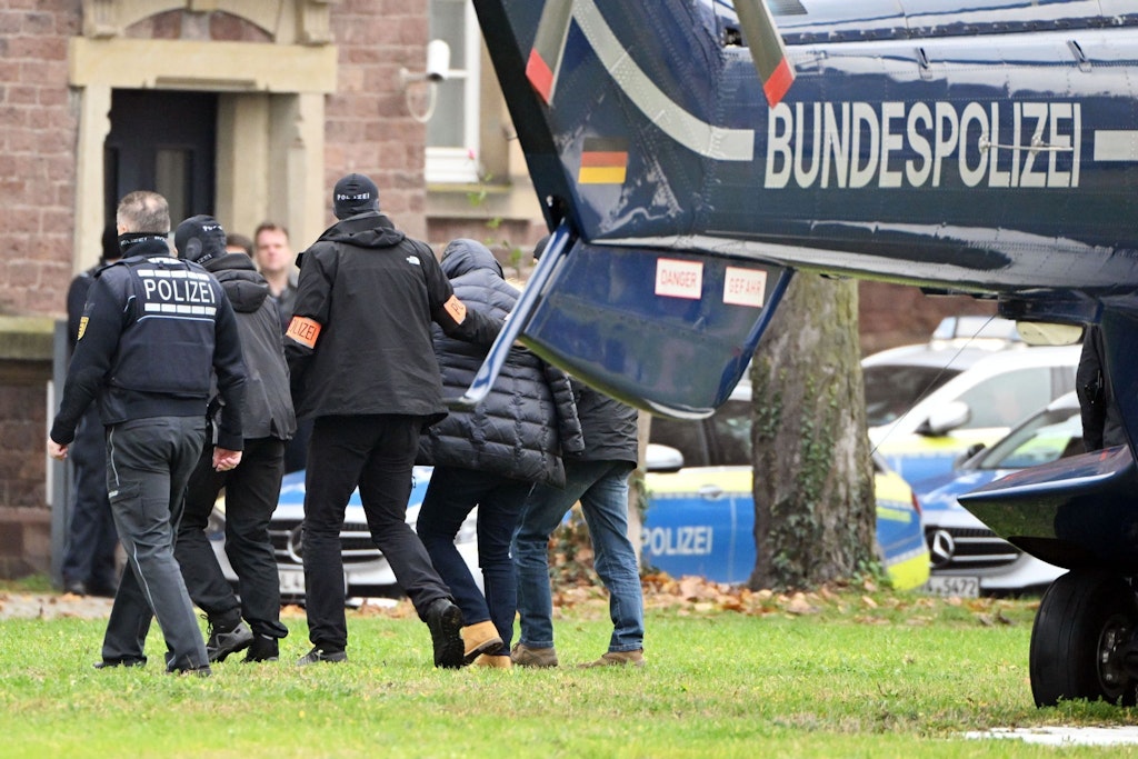 Eine Person (2.v.r.) wird von Polizisten aus einem Hubschrauber gebracht.