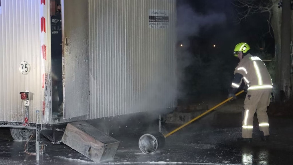 Ein Feuerwehrmann rollt die Propangasflasche mit einer Stange vom Bauwagen weg - in diesem Moment öffnet der Wachmann (73) von innen die Tür. Davor liegt der Gasofen, den er brennend aus dem Wagen gekippt hatte.