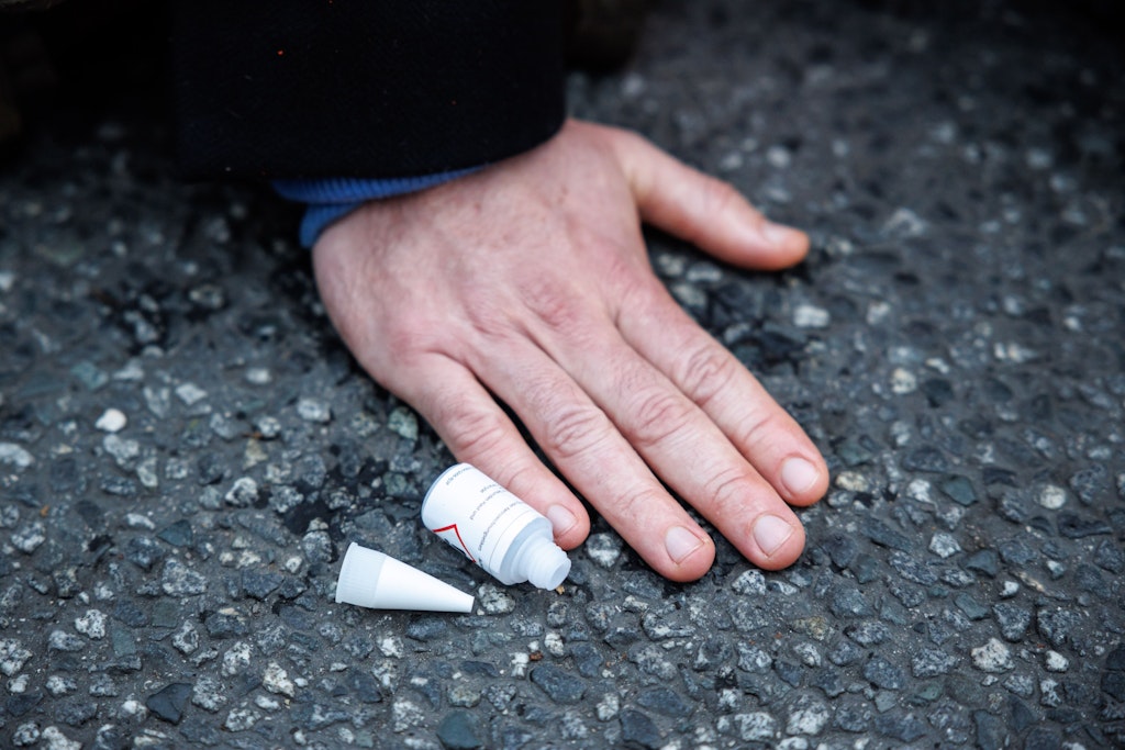 Ein Klima-Kleber hat sich auf einer Straße festgeklebt. Zu sehen ist die Flasche mit dem Klebstoff, den es un in einer Warenhauskette momentan nicht mehr gibt.