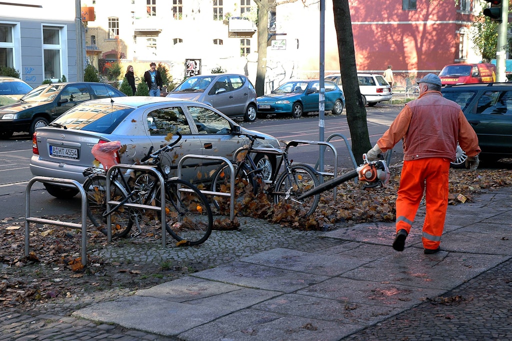 Ein BSR-Mitarbeiter „kehrt“ Laub mit einem Laubbläser vom Gehweg.