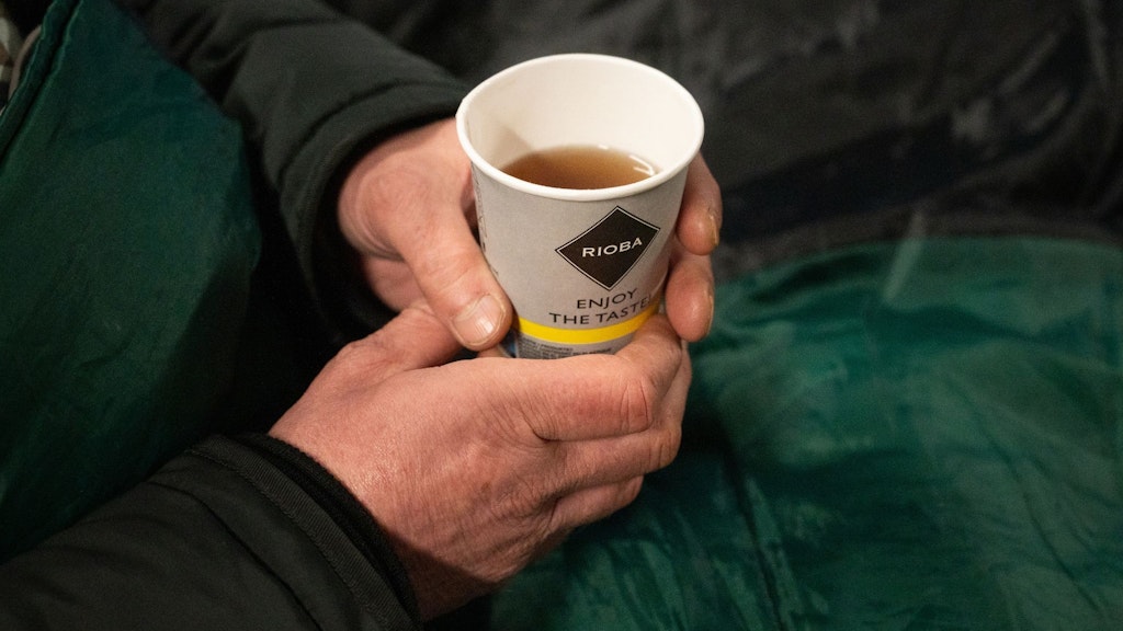 Ein Obdachloser hält einen Becher Tee in der Hand. 
