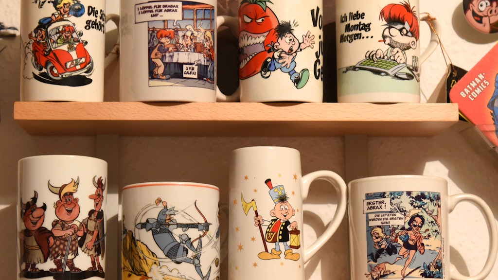 Im Regal stehen Tassen mit Motiven der Digedags und der Abrafaxe aus der Comiczeitschrift „Mosaik“.