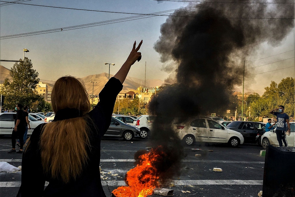 Eine Frau steht während einer Demonstration nach dem Tod der 22-jährigen Mahsa Amini vor einem brennenden Autoreifen und zeigt das Victory-Zeichen.