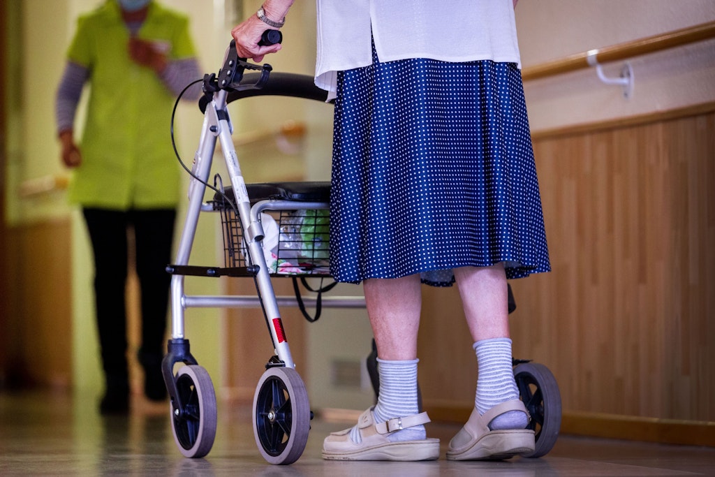Eine ältere Dame geht mit ihrem Rollator über den Flur eines Pflegeheims.