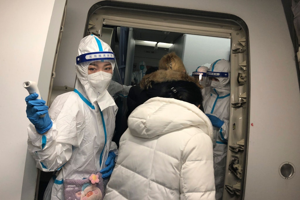 Kabinenpersonal in Schutzkleidung begrüßt Reisende auf dem Weg nach China an Bord eines Fluges vom JFK-Flughafen und prüft deren Temperatur.