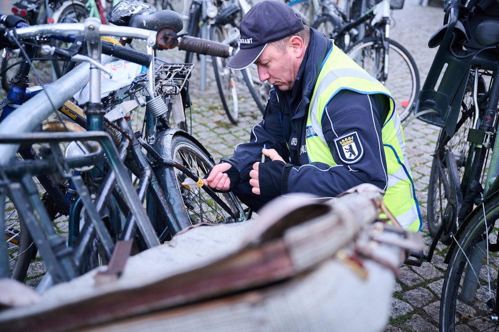 Ein Mitarbeiter vom Ordnungsamt Berlin-Mitte befestigt einen gelben Zettel an einem mutmaßlich herrenlosen Fahrrad. Auf dem Zettel steht der Hinweis, dass das Rad durch eine lange Standzeit aufgefallen ist, der Eigentümer wird aufgefordert, es wegzuräumen.