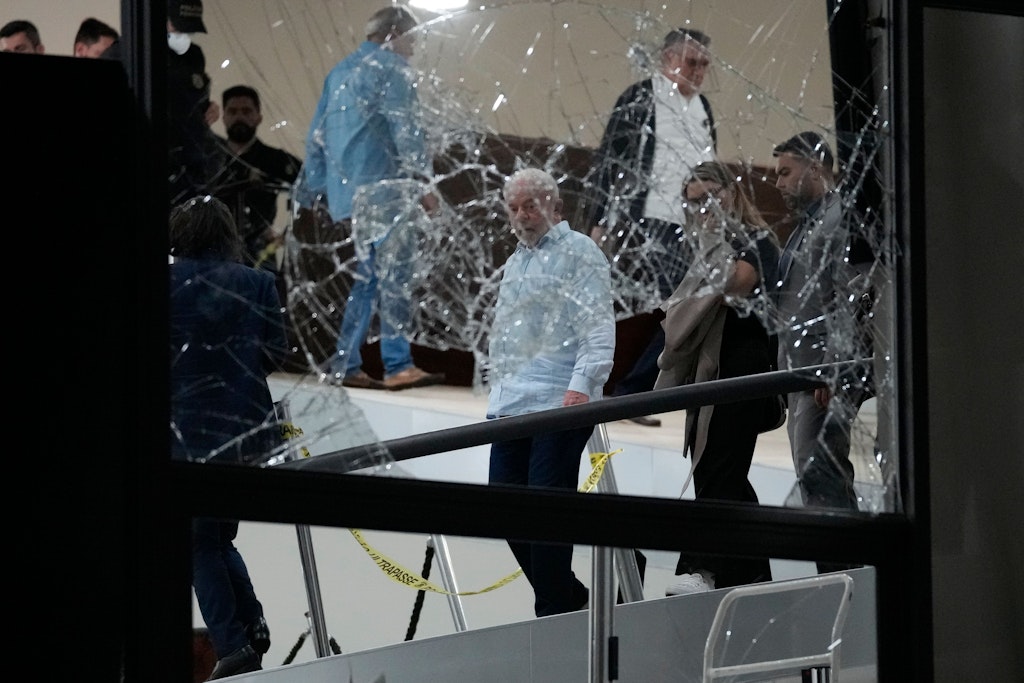 Brasiliens Präsident Lula da Silva im blauen Hemd hinter einer zertrümmerten Scheibe im Präsidentenpalast. Er war während des Angriffs auf einer Dienstreise. 