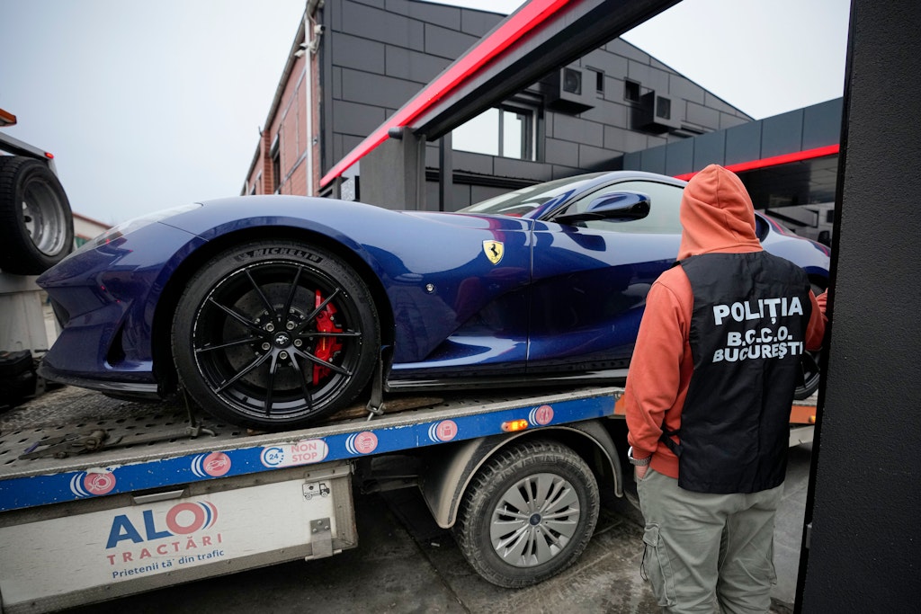 Ein Polizeibeamter überwacht, wie ein Ferrari, der im Rahmen eines Verfahrens gegen den wegen Verdachts auf Menschenhandel, Geldwäsche und Vergewaltigung inhaftierten Medien-Influencer Andrew Tate beschlagnahmt wurde, abgeschleppt wird.