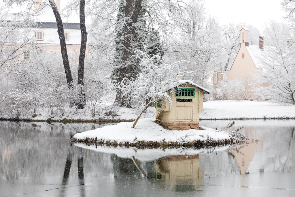 Vor dem Schloss im Branitzer Park spiegelt sich in verschneiter Landschaft ein Miniaturhäuschen. Laut Wetter-Experten wird es wieder kälter.